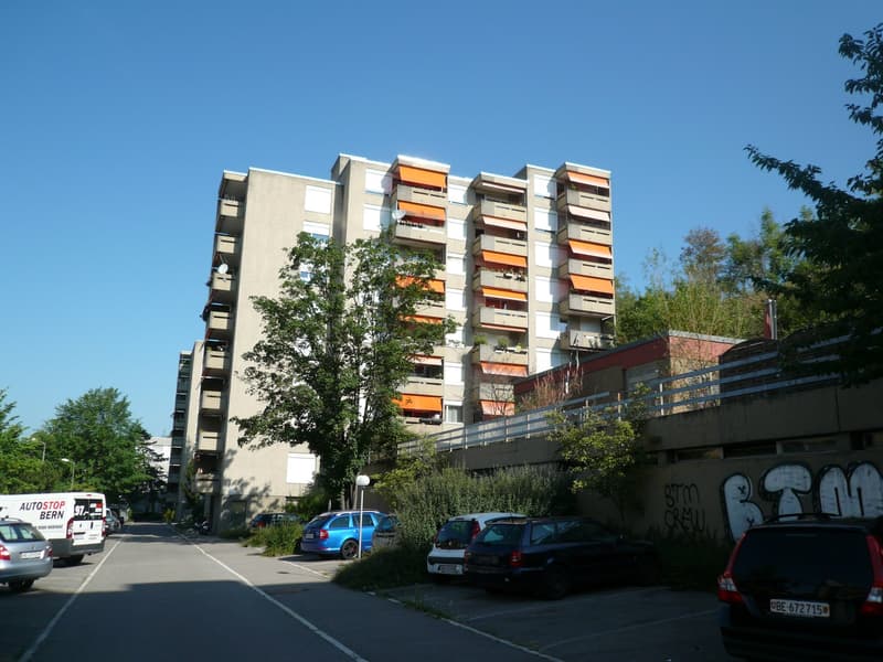 Multi-story apartment building with balconies, cars parked in front