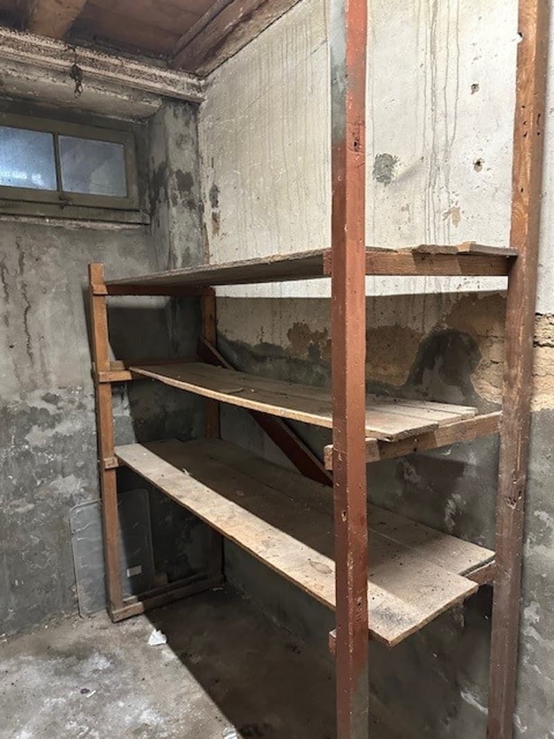A storage room with wooden shelves on the wall and cement walls.