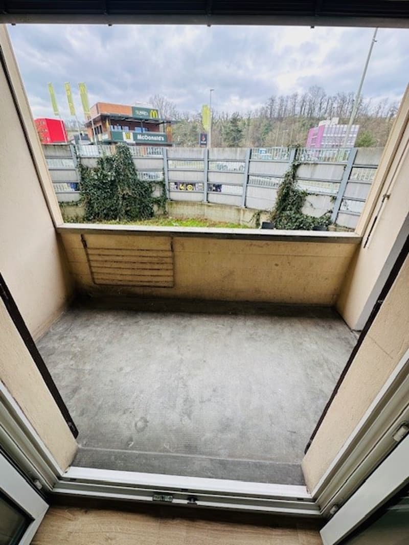 An open balcony with a concrete floor and a view of a road and trees.