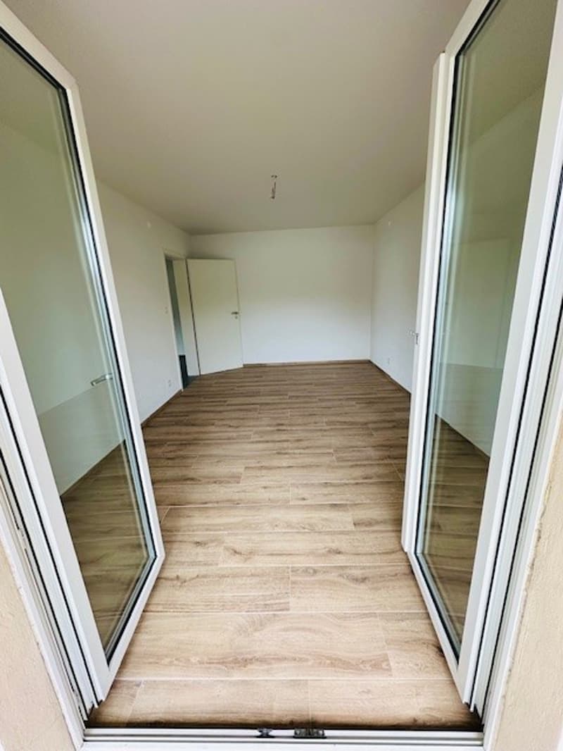 Empty room with wooden floor, glass doors, white walls, and a white door.