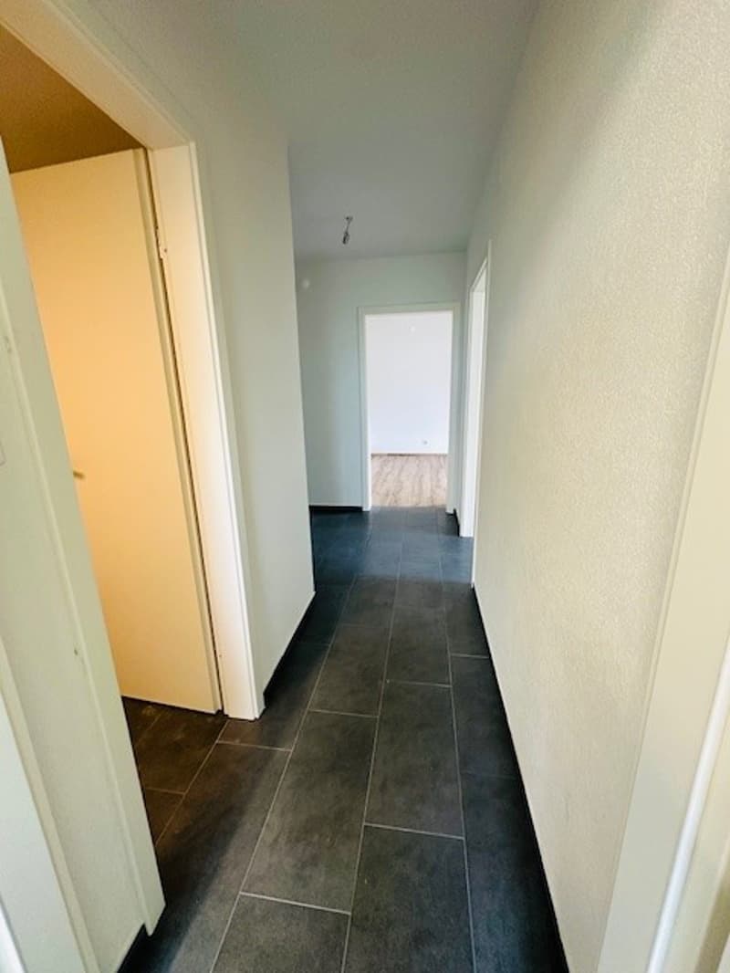Empty hallway with white walls, black tiles, and doors on both sides.