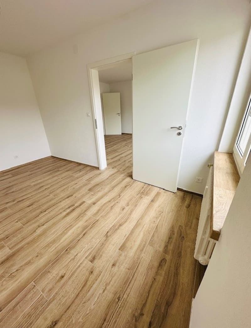 Empty room with wooden floors, white walls, and two doors leading to another room.