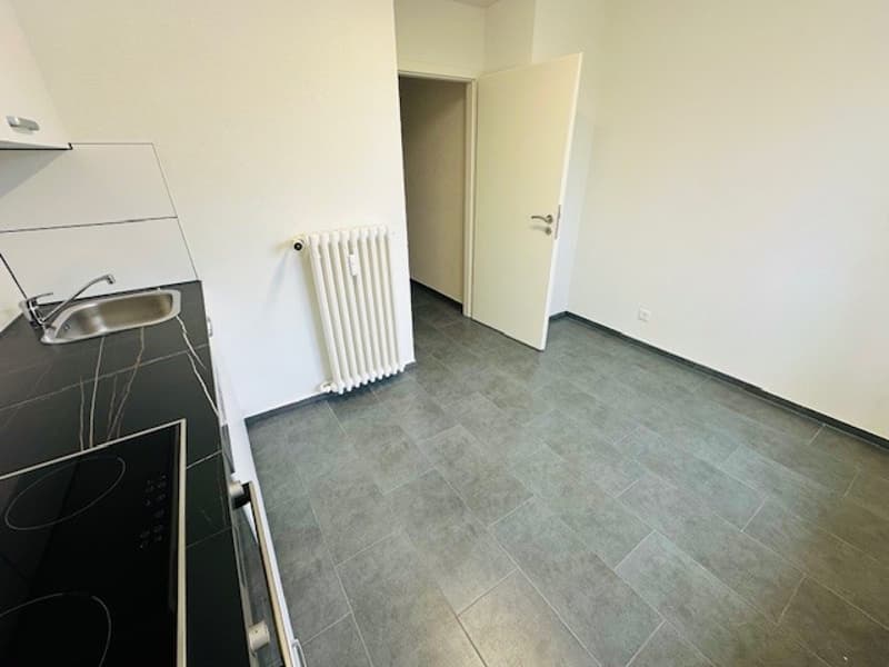 Empty kitchen with white walls, black countertop, silver sink, white radiator, open door
