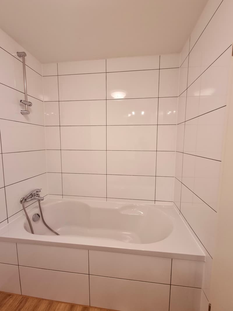 Bathroom with white tiles, bathtub, shower head, wooden floor