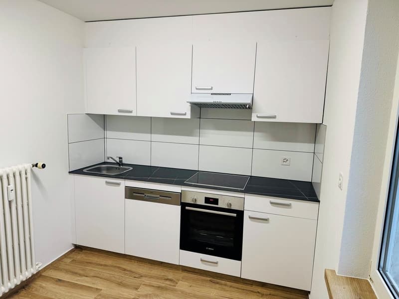 modern kitchen with white cabinets, black countertops, integrated dishwasher, oven, and sink with faucet