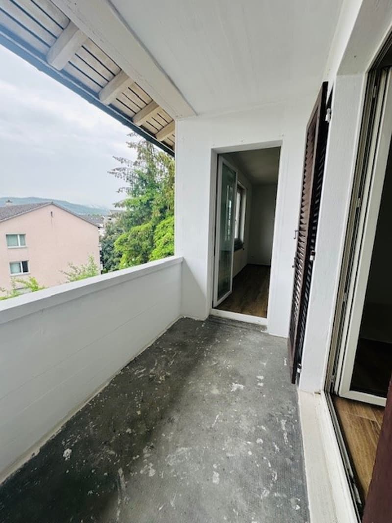 empty balcony with white walls, wooden floor, glass doors, view of trees and buildings