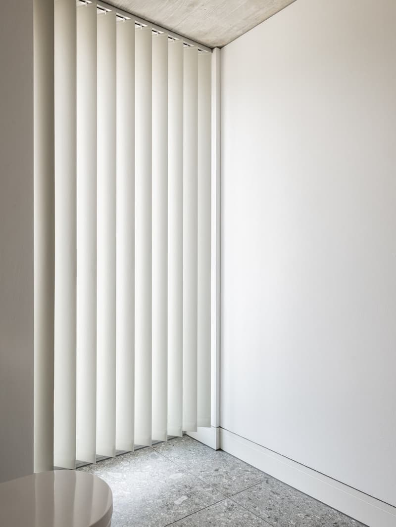minimalist bathroom with white walls, horizontal blinds, grey tiled floor, round toilet bowl