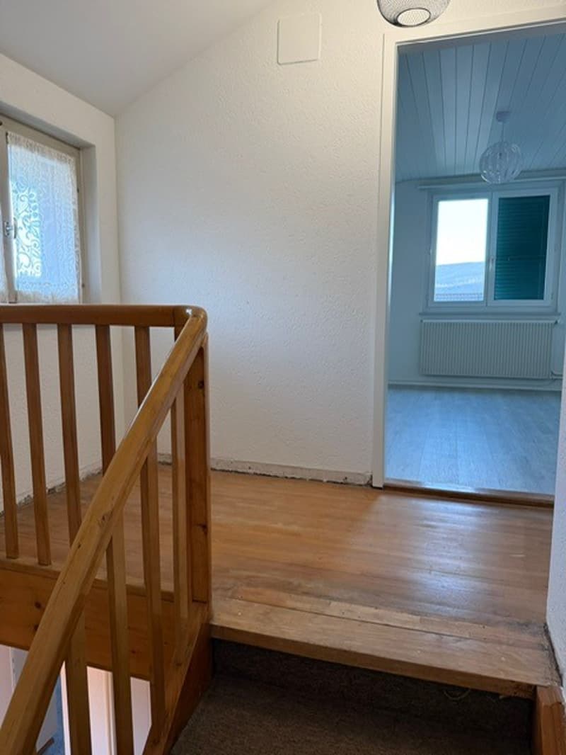 wooden stairs, white walls, carpet floor, window with curtains, radiator, lamp