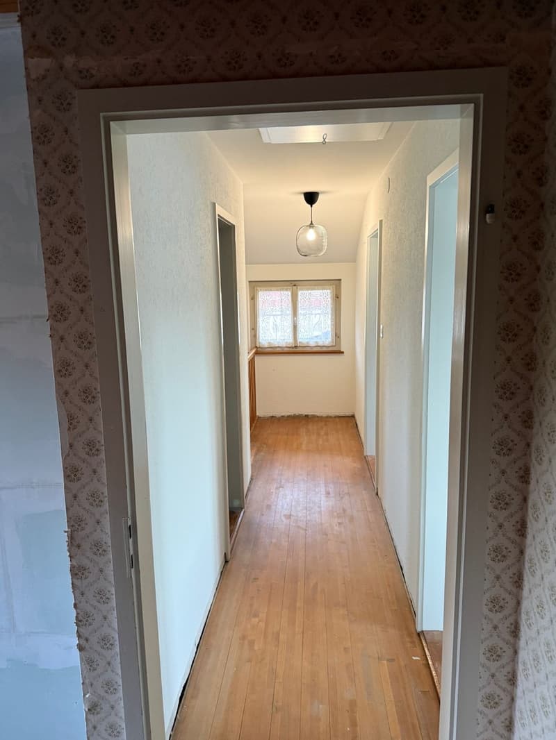 wooden floor, white walls, two doors on the right, skylight, window at the end