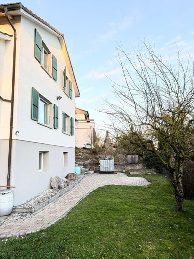 2 story house, white wall, green shutters, brick path, yard with grass, tree, storage container