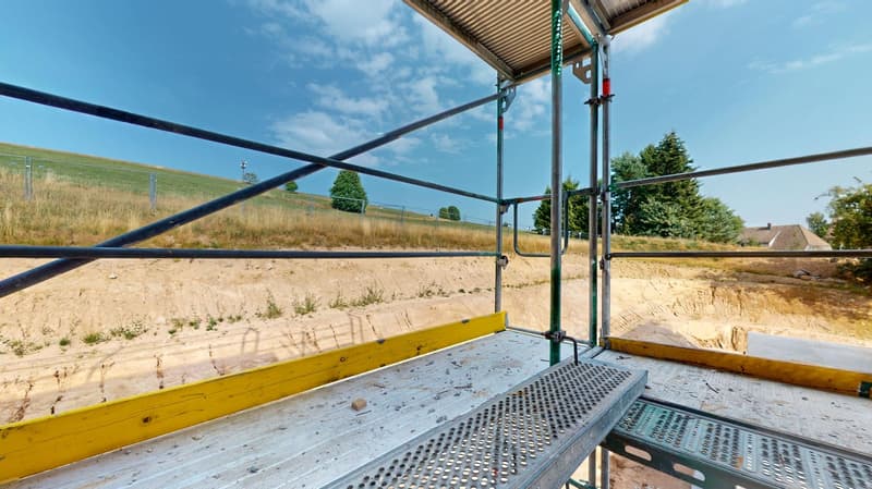 metal scaffolding, ground being prepared, field in the background, trees in the background
