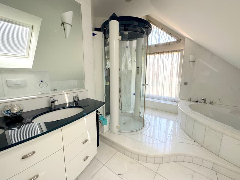 modern bathroom with white tiles, a glass walk-in shower, freestanding tub, sink with a faucet, white vanity cabinets, large mirror, wall-mounted sconces, and a window with blinds
