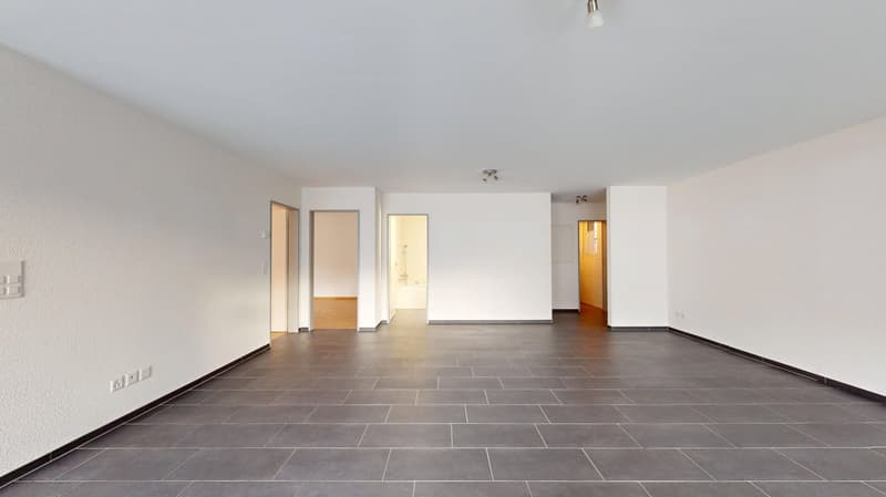 Empty room, white walls, tile floor, several doors, wall mounted power outlets, wall mounted lights