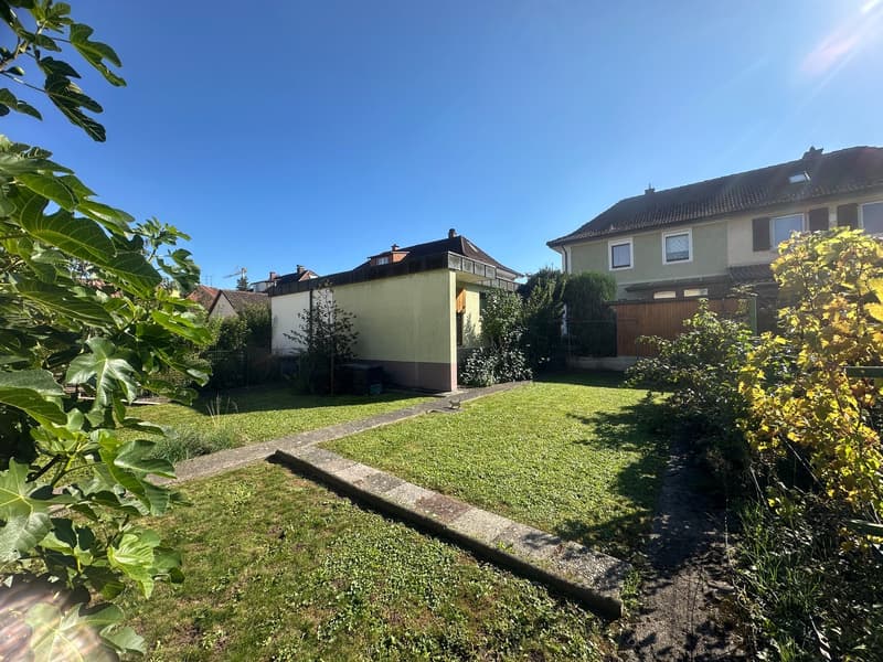 A backyard with green lawn and plants, a pathway leading to the house, and a blue sky background.