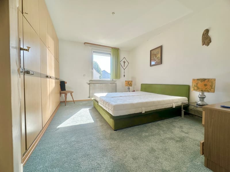 large double bed, green bed base, nightstands with lamps, wooden cabinet, built-in wardrobe, radiator, picture frame, cross pendant
