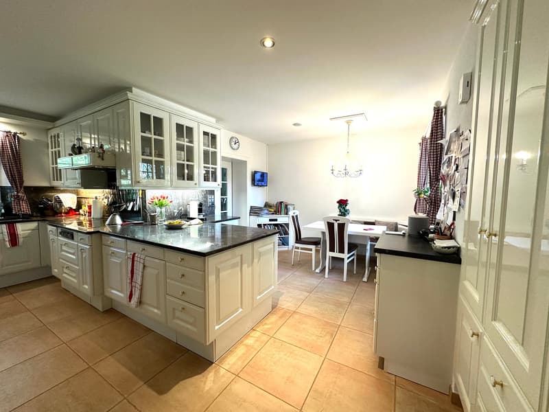 Open plan kitchen with white cabinets, black granite countertops, dining area with white table and chairs, white refrigerator, black dishwasher, white cabinets and drawers, microwave and clock, chandelier