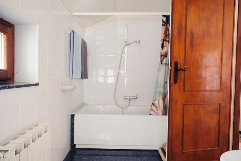 White bathroom with white tiles, shower, bathtub, white heater