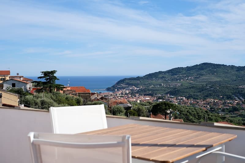 Outdoor balcony with table and chairs, large window, view over houses and town, ocean, hills
