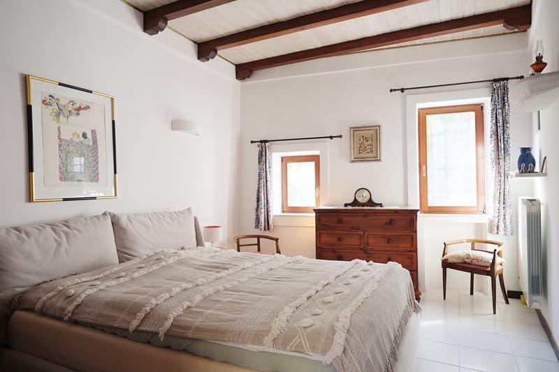 Bedroom with a bed, wooden dresser, wooden chair, lamp, radiator, framed artwork, and curtains
