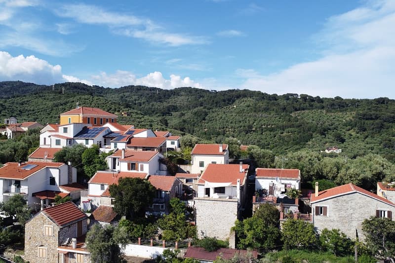 Cluster of buildings with red roofs set against a backdrop of lush green hills.