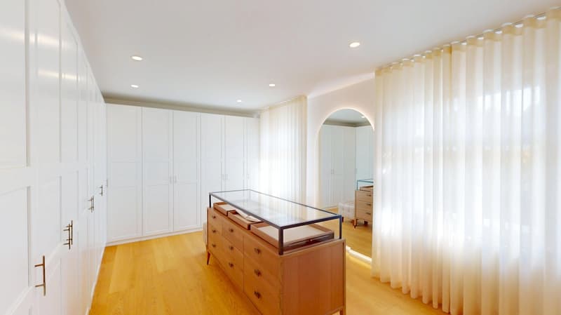 a room with tall white wardrobes, a wooden dresser with a glass top, and white curtains