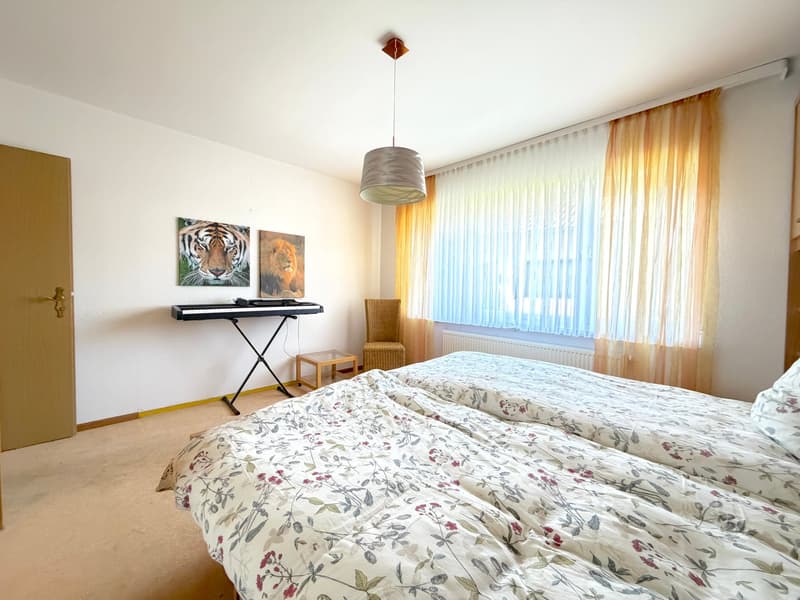 Bedroom with two beds, piano, chair, radiator, curtains, tiger and lion paintings, wooden door