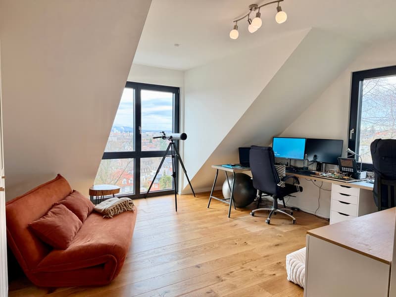 A room with a desk, two monitors, a telescope, a couch, and a view of the city.