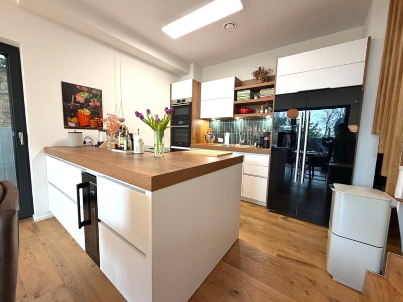 modern kitchen with white cabinets, wooden countertop, black appliances, wooden floor, white walls, central island, flowers, trash bin
