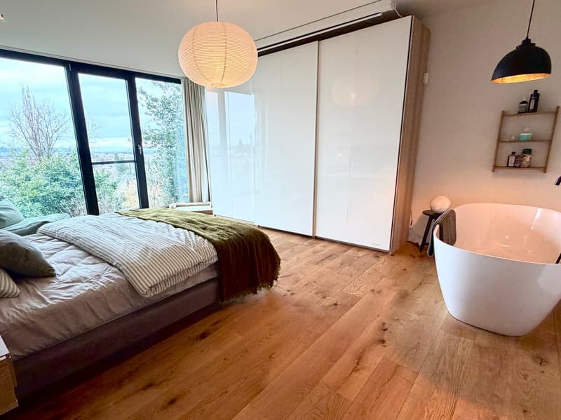 Bedroom with bed, wooden floor, large windows, bathtub, lamps, closet