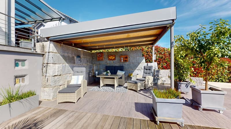 Outdoor seating area with a canopy, stone walls, wooden floor, wicker chairs, table, and potted plants
