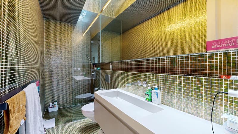 modern bathroom with glass shower, white sink, yellow and green tiled walls, towel rack, toilet