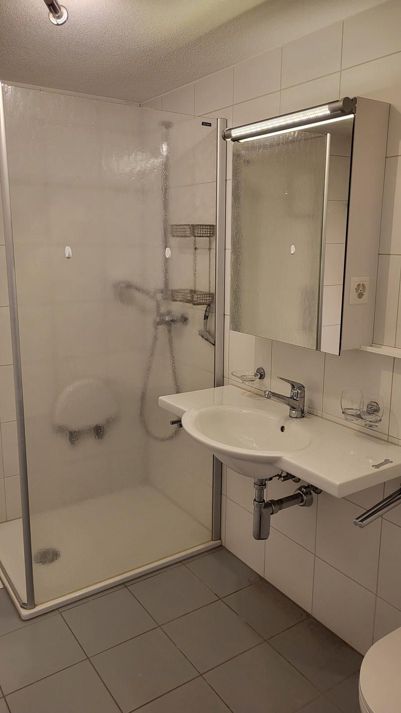 tiled floor, glass shower enclosure, white vanity, silver faucet, white tiles, soap dish, mirror with lights