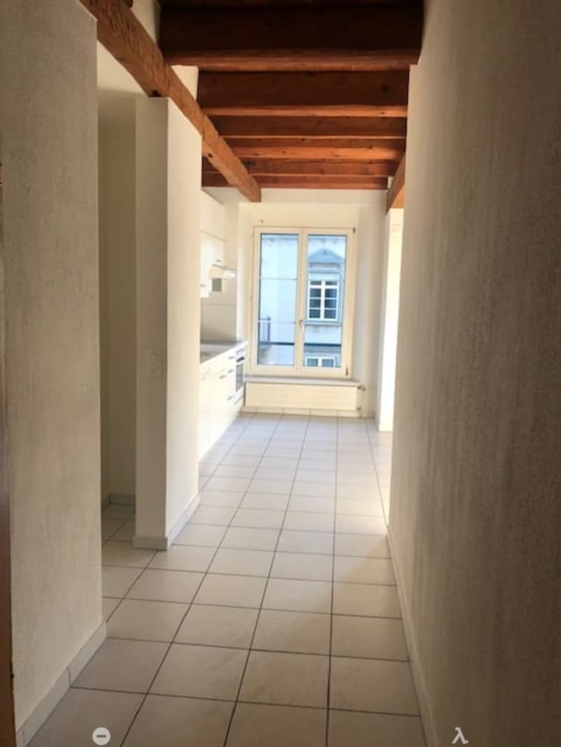 tiled hallway with wooden ceiling beams, kitchen with windows and appliances, small room with an additional window