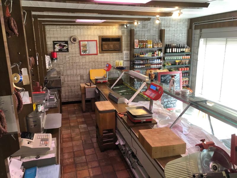 The image shows a commercial kitchen or food preparation area. It has tiled walls, shelves with various food items and cooking equipment, a cash register, and a dishwasher visible.