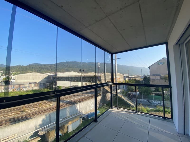Modern apartment balcony with glass panels, view of railway and mountains