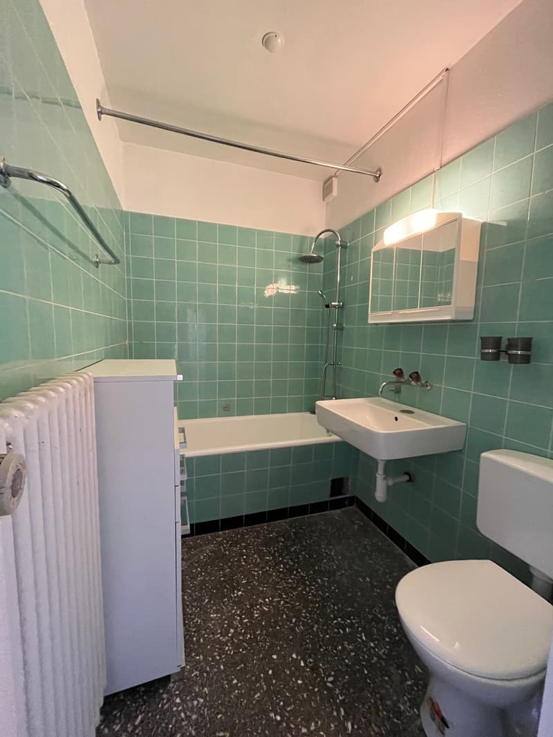 Bathroom with teal tiles, white fixtures, bathtub, sink, and toilet.