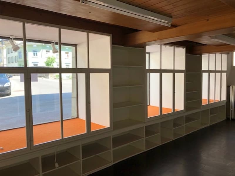 large windows, ceiling-mounted track lighting, open floor plan, built-in shelves, exposed wooden ceiling