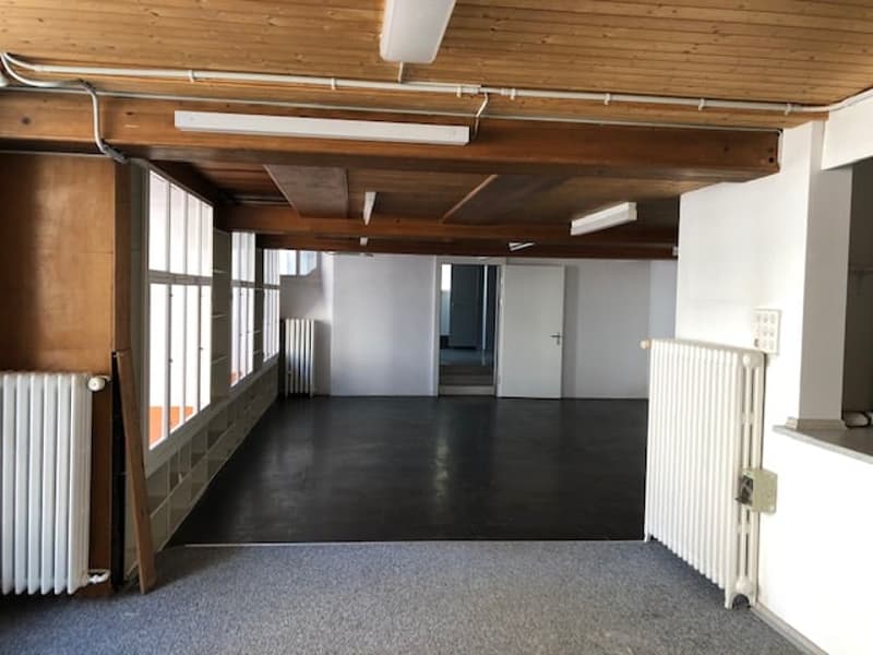 Empty room, wooden ceiling, large windows, two radiators, wooden beam, tiled floor, open door.
