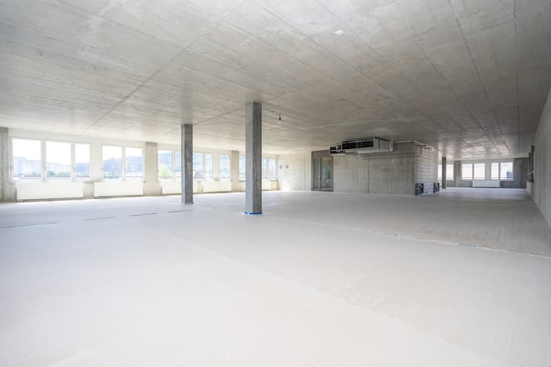 Empty room with white walls and ceiling, four pillars in the middle, windows on one side, and an air conditioning unit on the wall