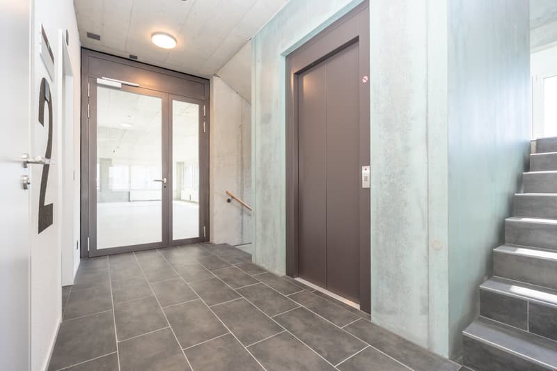 Stainless steel railing, tiled flooring, glass doors, number 2 sign, white walls, elevator shaft