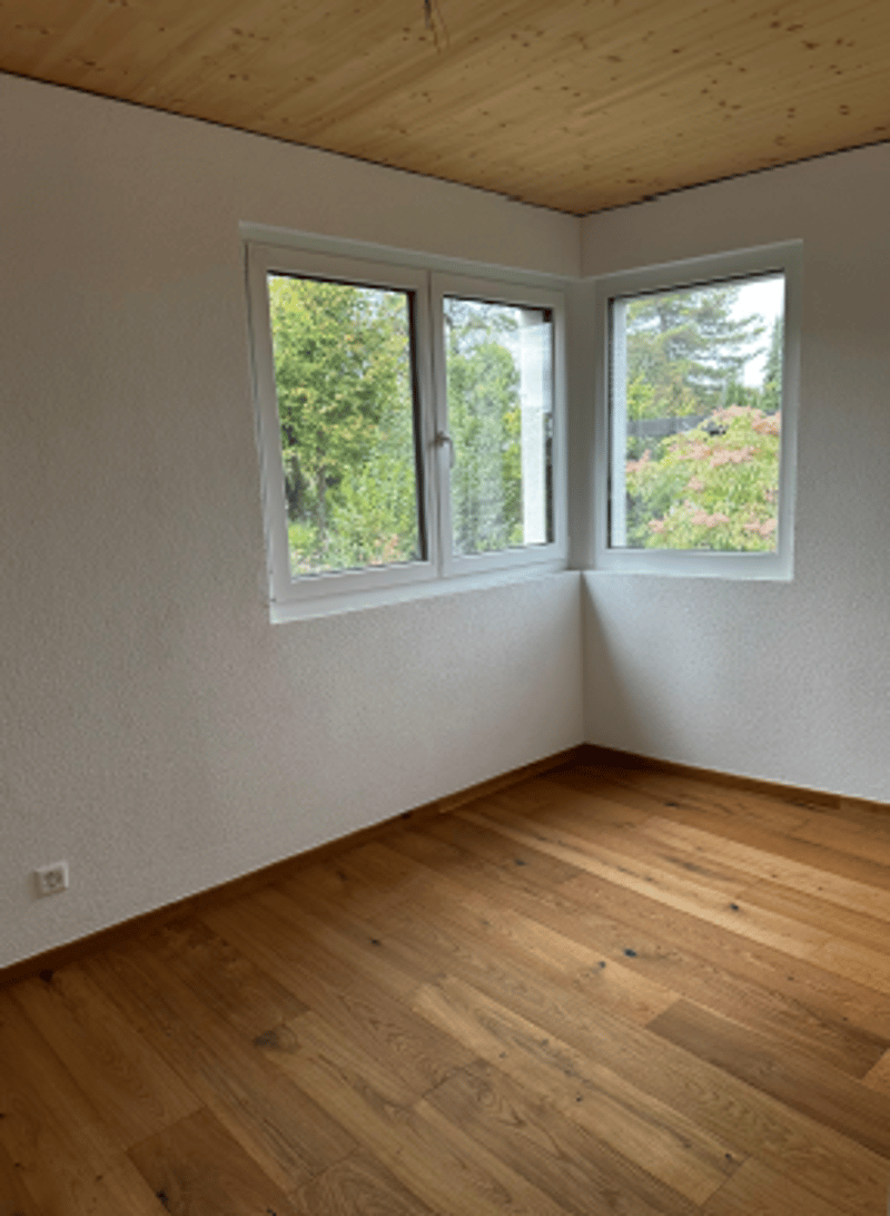 Empty room with wooden floors, white walls, 2 windows, and a wooden ceiling.