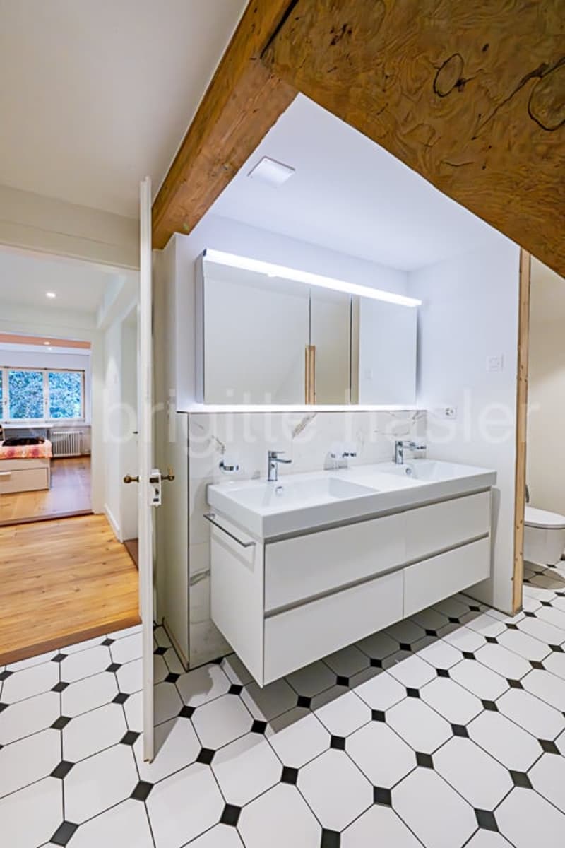 Spacious bathroom with a double vanity sink, large mirror, and a tiled floor with a black and white geometric pattern.