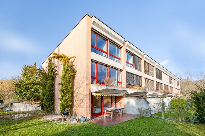 Modern building, pink exterior, red window frames, outdoor dining table, garden, small porch, shrubs and trees