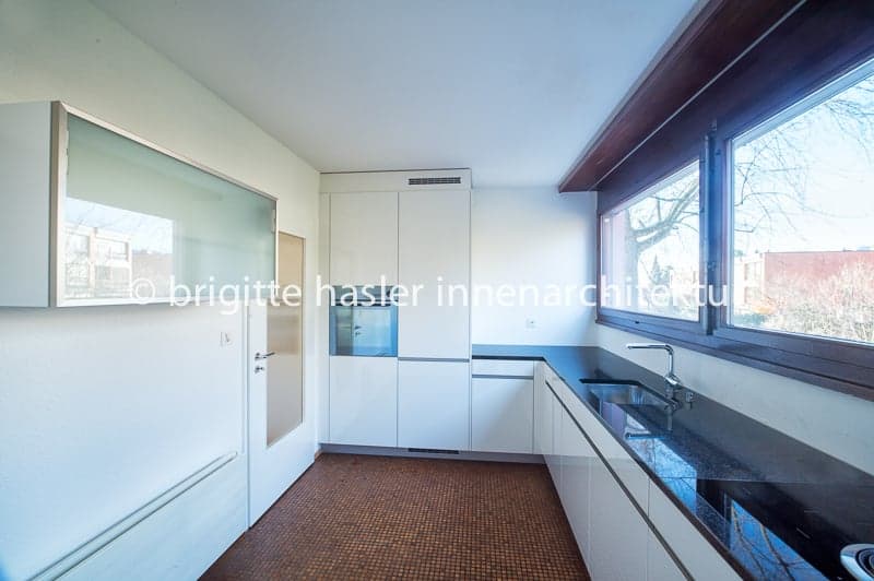 modern kitchen with white cabinets, black countertops, stainless steel sink, large windows