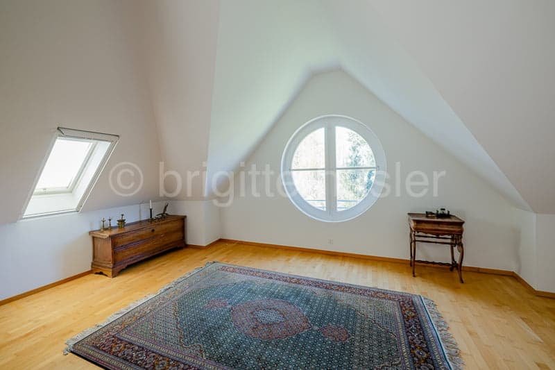 wooden floor, white walls, two windows, round window, wooden cabinet, wooden table, rug