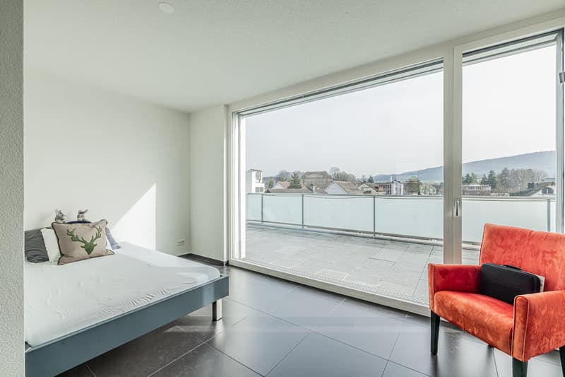 single bed, white sheets, pillows, chair, large windows, balcony