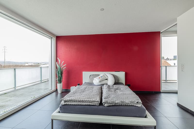 bedroom with red wall, large windows, balcony, bed, pillows, blankets, potted plant