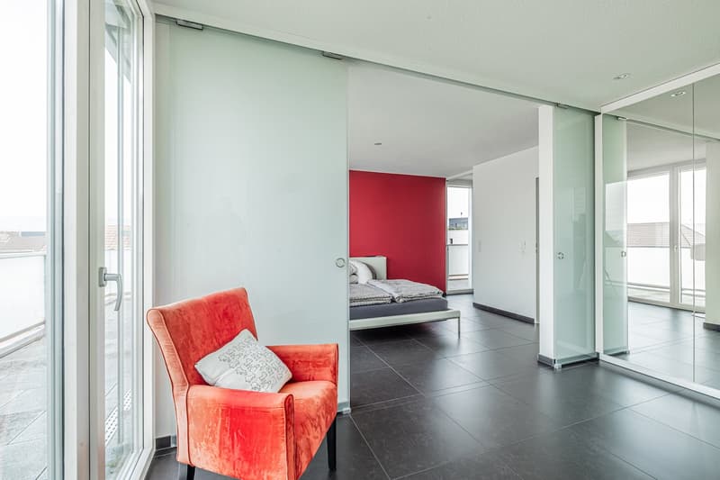 modern room with glass walls, black tiles, red chair, white pillow, glass door, bed, red wall