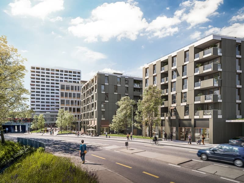 Modern multi-story apartment buildings with balconies, surrounded by trees and pedestrian walkways. The buildings have a mix of materials including glass, metal, and concrete. There are people walking and riding bicycles on the street in front of the buil