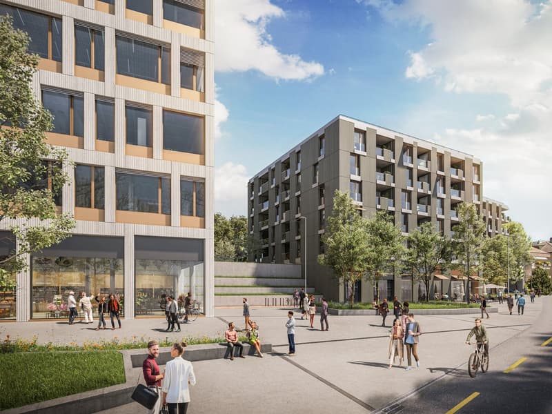 Multi-story apartment building with modern, angular architecture, large windows, and balconies. Ground floor has retail spaces. Outdoor plaza with benches and landscaping, with people walking and relaxing in the area.